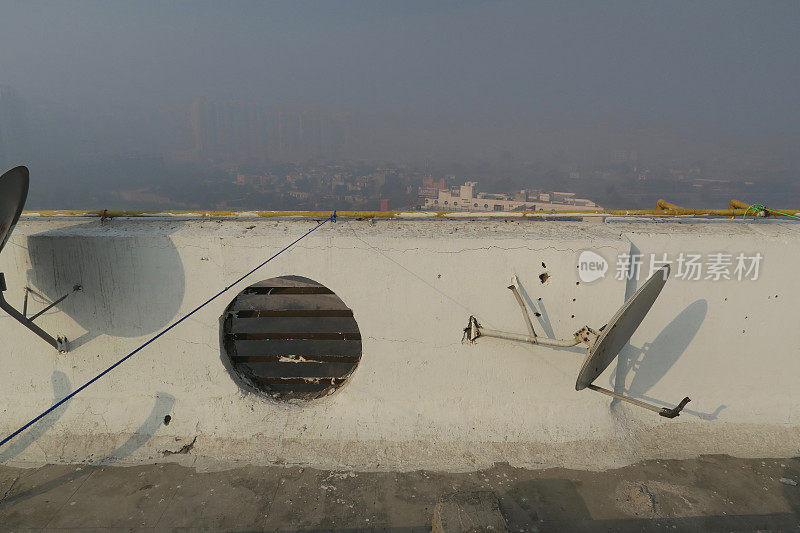印度北方邦新德里的印度公寓楼屋顶的图片，通过墙上的洞显示早晨雾蒙蒙的天空污染，被污染的雾蒙蒙的天空，德里污染的照片汽车尾气/工厂排放